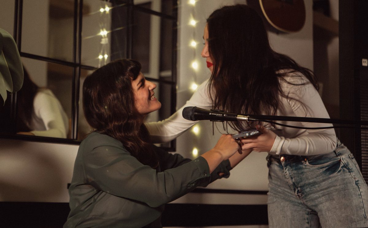 Two women sharing a microphone at Casa Corah
